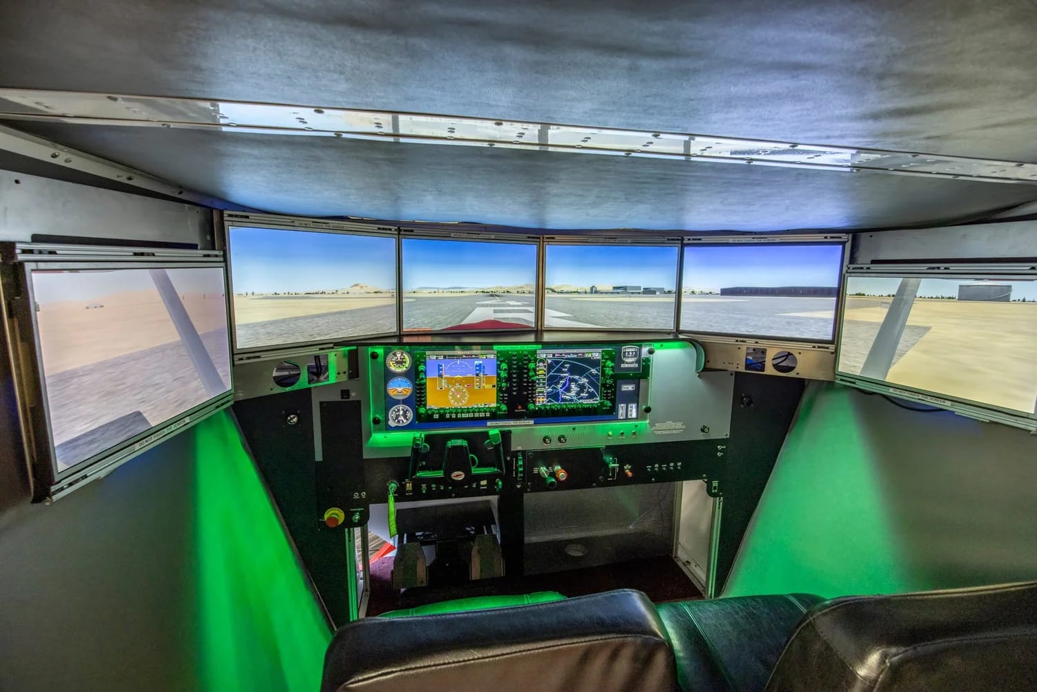 Inside the Redbird FMX cockpit at night — six wraparound visual screens showing a runway, twin glass-cockpit displays, dual yokes, and atmospheric green lighting