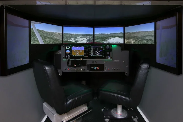 Side-by-side twin pilot seats inside the FMX cockpit with curved wraparound visual screens and a glass-cockpit panel