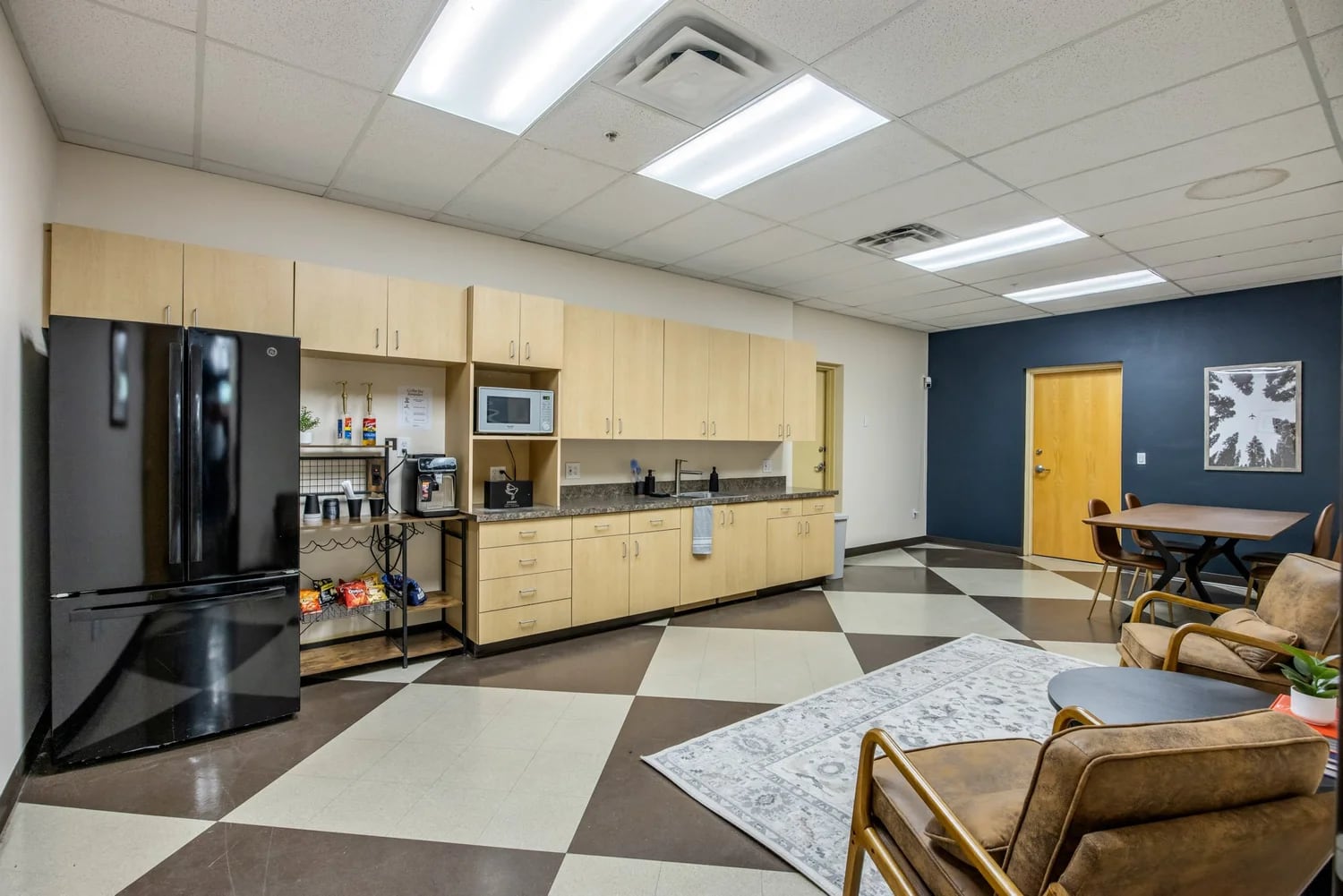 Member kitchen and lounge — full-size fridge, microwave, espresso bar, prep counter, and a casual seating area at the far end