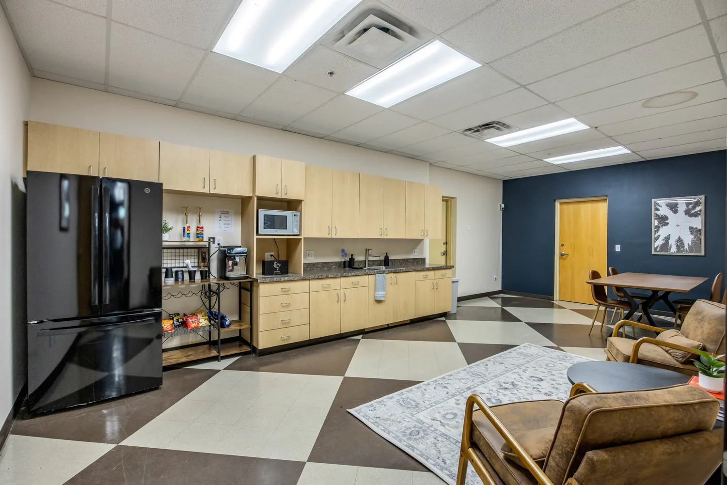 Member kitchen and lounge — full-size fridge, microwave, espresso bar, prep counter, and a casual seating area at the far end